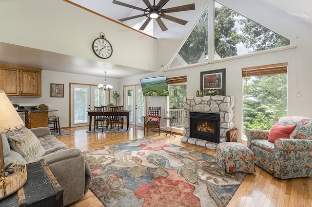 living room featuring a fireplace, light wood-style flooring, ceiling fan with notable chandelier, and a high ceiling