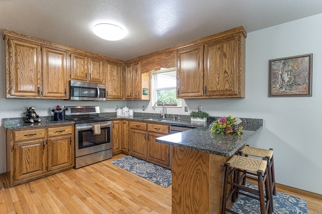 kitchen featuring brown cabinetry, appliances with stainless steel finishes, a peninsula, and a sink