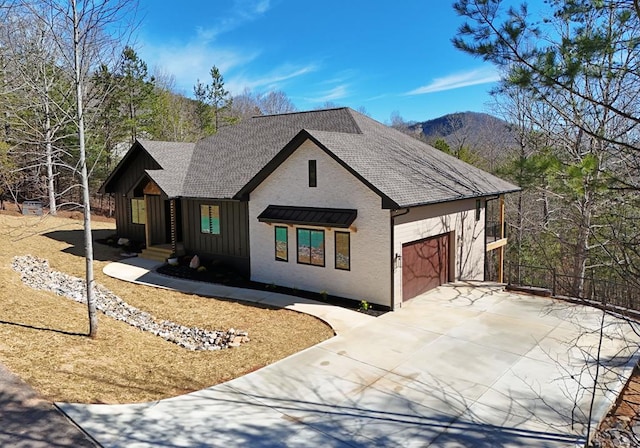 modern farmhouse style home featuring a shingled roof, concrete driveway, an attached garage, board and batten siding, and a mountain view