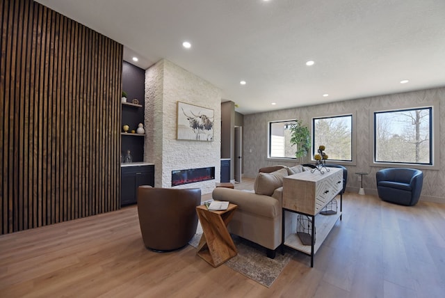 living area featuring light wood finished floors, recessed lighting, built in features, and a stone fireplace