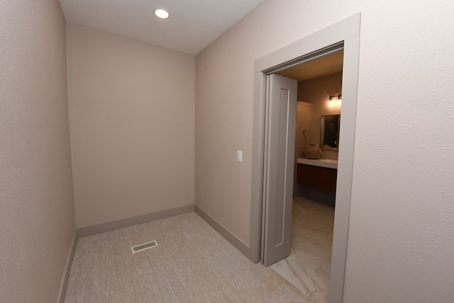 hall featuring light carpet, baseboards, visible vents, and a textured wall