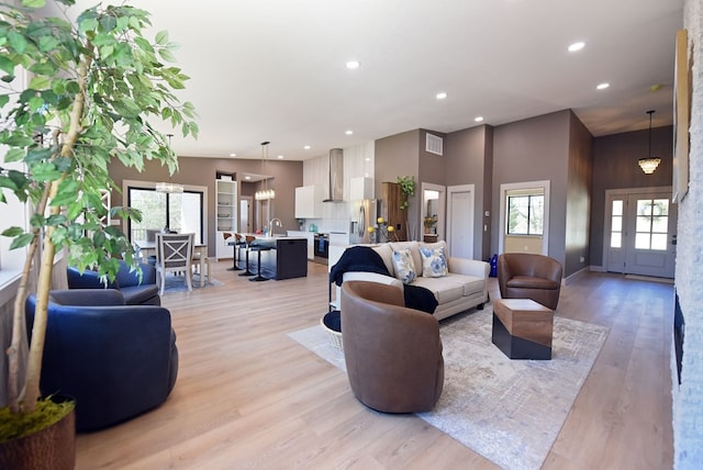 living room with light wood finished floors, a towering ceiling, visible vents, and recessed lighting