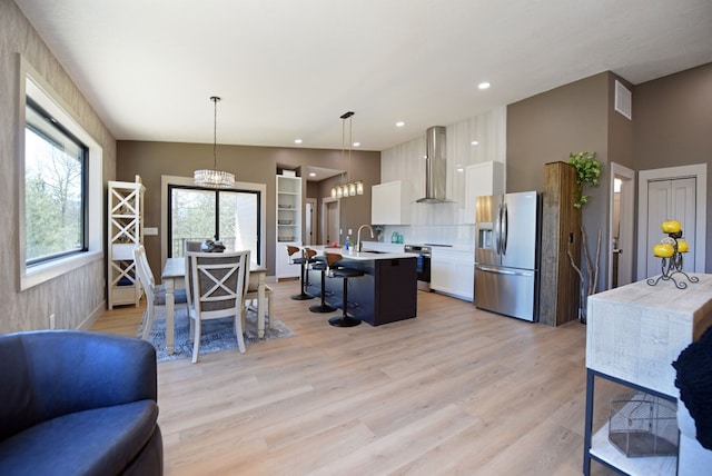 kitchen featuring stainless steel appliances, a breakfast bar, white cabinets, light countertops, and wall chimney exhaust hood