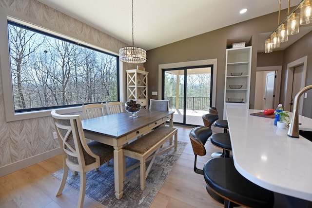 dining space with lofted ceiling, a notable chandelier, baseboards, light wood-type flooring, and wallpapered walls