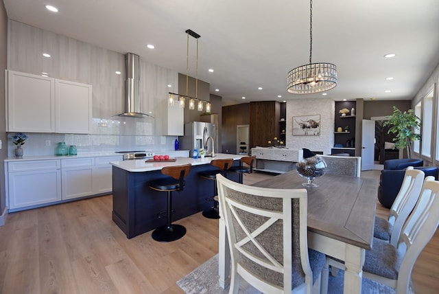 kitchen with white cabinets, light wood-style floors, light countertops, appliances with stainless steel finishes, and wall chimney range hood