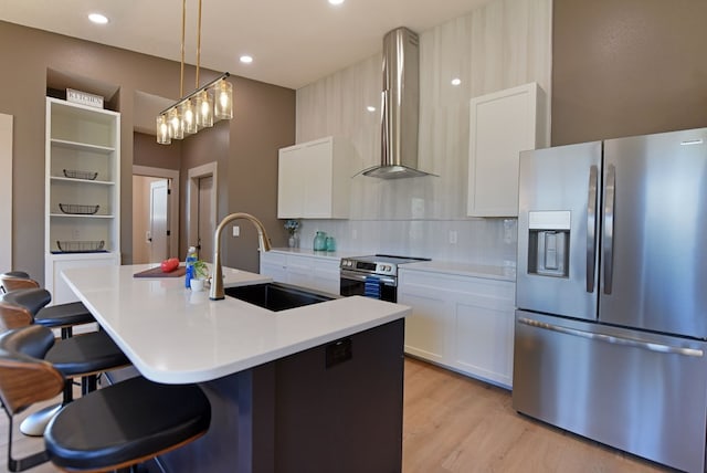 kitchen with light wood finished floors, stainless steel appliances, a kitchen bar, a sink, and wall chimney exhaust hood