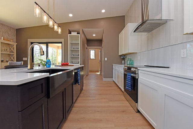 kitchen featuring light countertops, light wood-style flooring, appliances with stainless steel finishes, white cabinets, and wall chimney exhaust hood