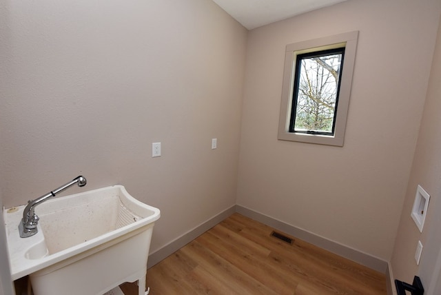 washroom featuring laundry area, a sink, visible vents, baseboards, and light wood-type flooring