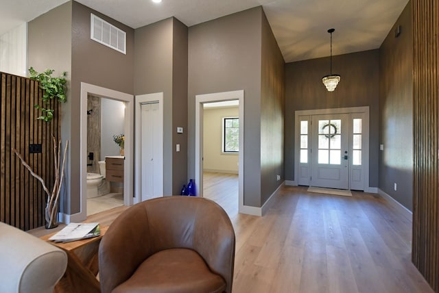 entryway with baseboards, visible vents, light wood-style flooring, and a high ceiling