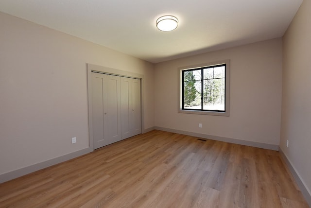 unfurnished bedroom featuring light wood finished floors, baseboards, and a closet