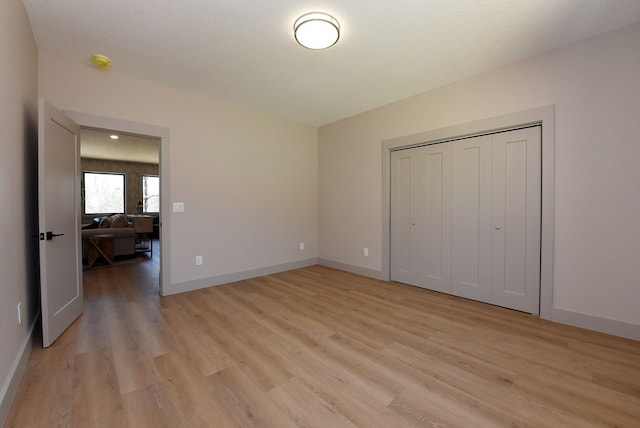 unfurnished bedroom featuring light wood-type flooring, a closet, and baseboards