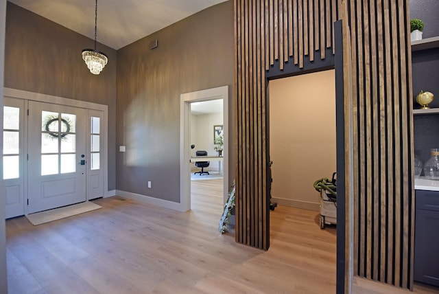 foyer featuring light wood-type flooring, baseboards, high vaulted ceiling, and a chandelier