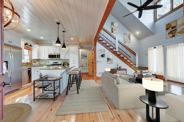 living room with wood ceiling, ceiling fan, wooden walls, sink, and light hardwood / wood-style floors