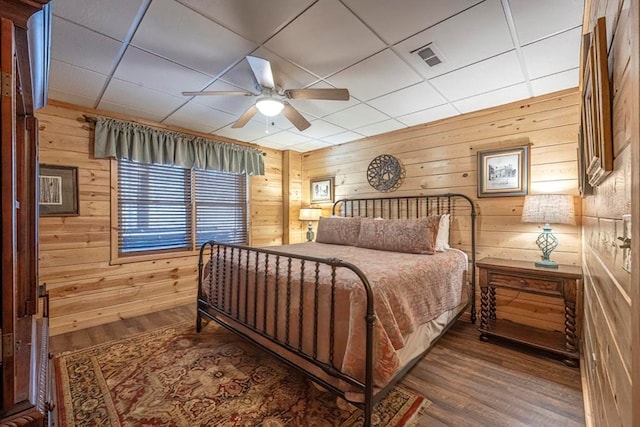 bedroom featuring visible vents, ceiling fan, wooden walls, and wood finished floors