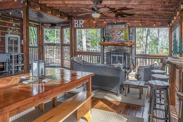 sunroom featuring ceiling fan and a stone fireplace