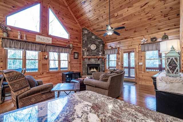 living room with a stone fireplace, wood finished floors, wood ceiling, and wooden walls