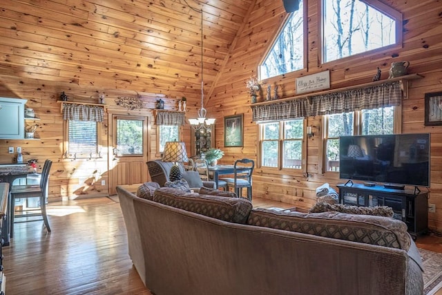 living area featuring high vaulted ceiling, wooden walls, an inviting chandelier, and wood finished floors