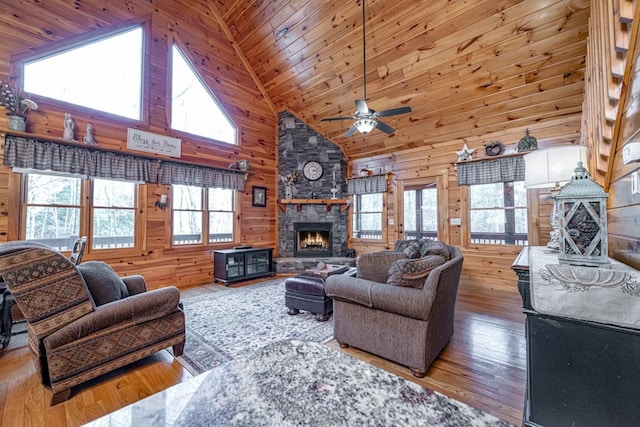 living area with a stone fireplace, plenty of natural light, and wooden walls