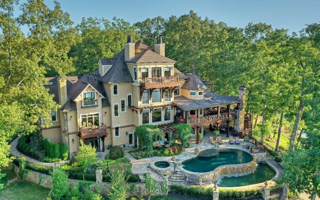 rear view of property with a balcony, a patio, and a swimming pool with hot tub