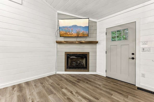 unfurnished living room featuring wood-type flooring, wooden walls, and vaulted ceiling