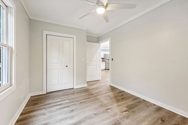 unfurnished bedroom featuring ceiling fan, ornamental molding, light wood-type flooring, and a closet