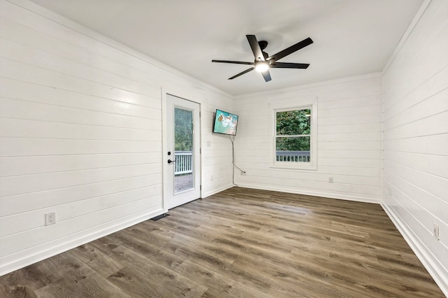 empty room featuring wood walls, ceiling fan, crown molding, and dark hardwood / wood-style flooring