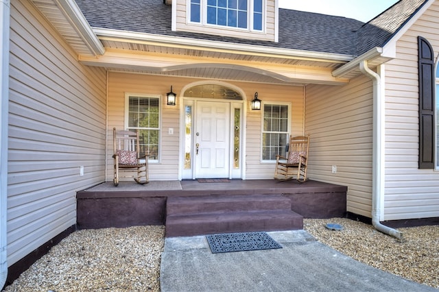 view of exterior entry with covered porch and a shingled roof