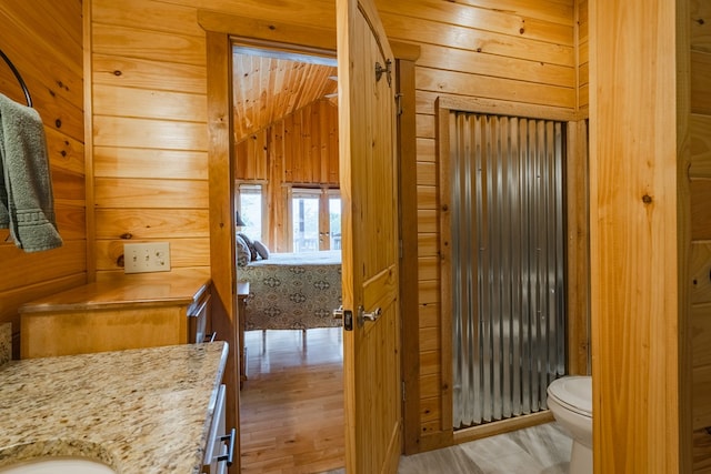 bathroom featuring hardwood / wood-style flooring, wooden walls, vaulted ceiling, toilet, and vanity