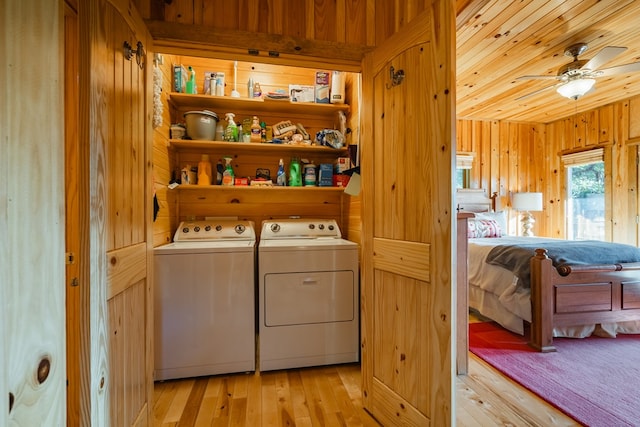 laundry room with wood walls, ceiling fan, washer and clothes dryer, and light hardwood / wood-style flooring