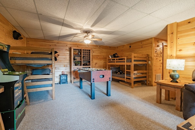 playroom with a paneled ceiling, wood walls, ceiling fan, and carpet