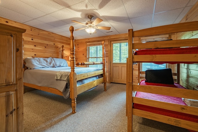 bedroom with a paneled ceiling, carpet, wood walls, and ceiling fan