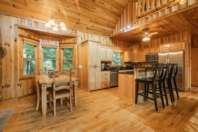 kitchen with appliances with stainless steel finishes, ceiling fan with notable chandelier, decorative light fixtures, and wooden walls