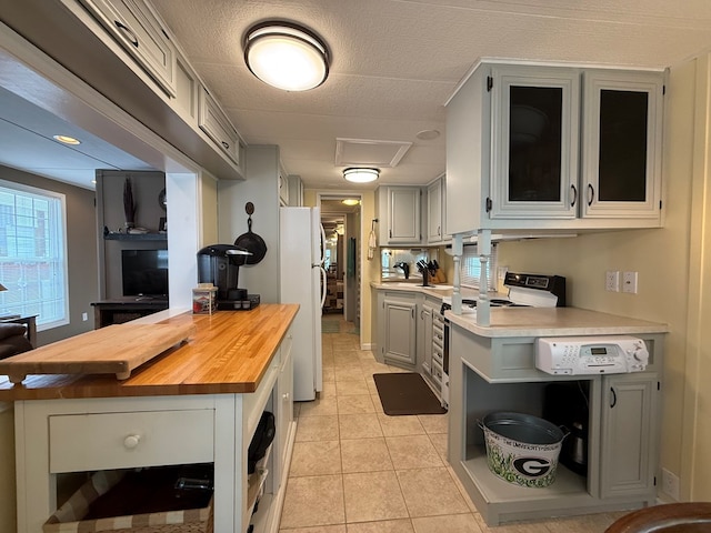 kitchen featuring open shelves, gray cabinets, freestanding refrigerator, butcher block counters, and range with electric stovetop