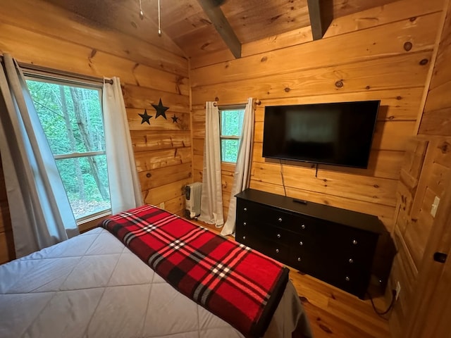 bedroom featuring radiator heating unit, hardwood / wood-style flooring, wooden walls, and multiple windows