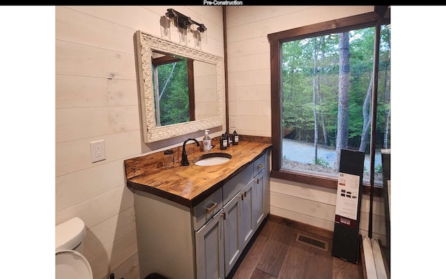 bathroom featuring hardwood / wood-style floors, vanity, a healthy amount of sunlight, and wooden walls