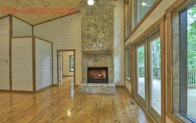 unfurnished living room with hardwood / wood-style floors, wooden ceiling, a stone fireplace, wooden walls, and ceiling fan