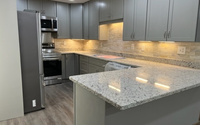 kitchen with stainless steel appliances, light stone countertops, a peninsula, and gray cabinets