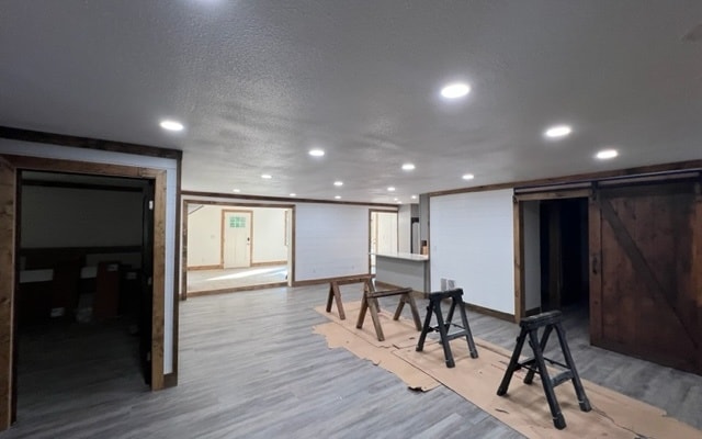 basement with light hardwood / wood-style flooring, a barn door, and a textured ceiling