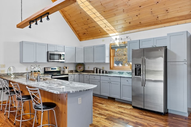 kitchen with kitchen peninsula, light stone countertops, high vaulted ceiling, light hardwood / wood-style flooring, and stainless steel appliances