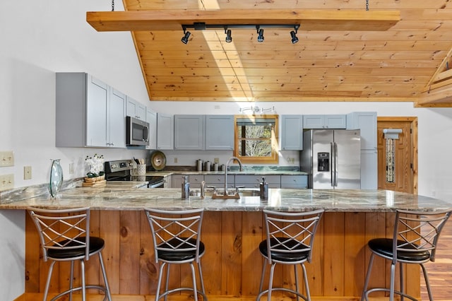 kitchen featuring light wood-type flooring, vaulted ceiling with beams, wood ceiling, kitchen peninsula, and stainless steel appliances