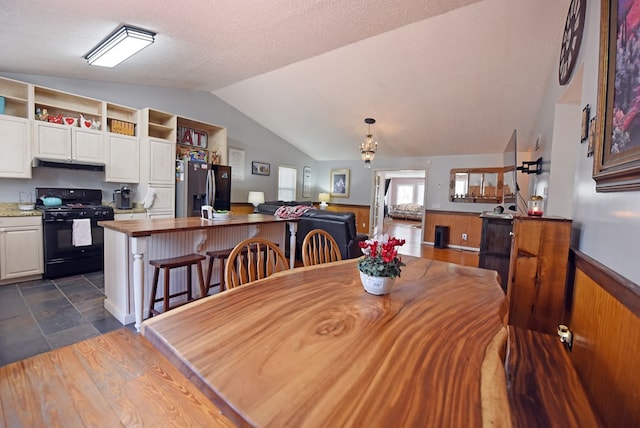 dining space with a wainscoted wall, a textured ceiling, and vaulted ceiling