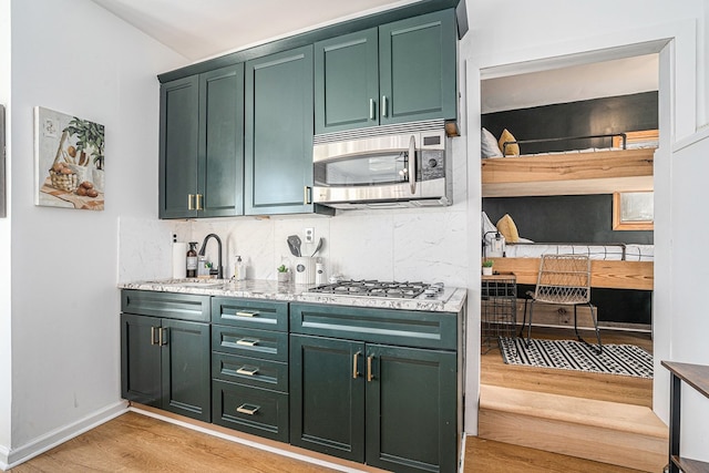 kitchen featuring sink, green cabinets, appliances with stainless steel finishes, backsplash, and light hardwood / wood-style floors