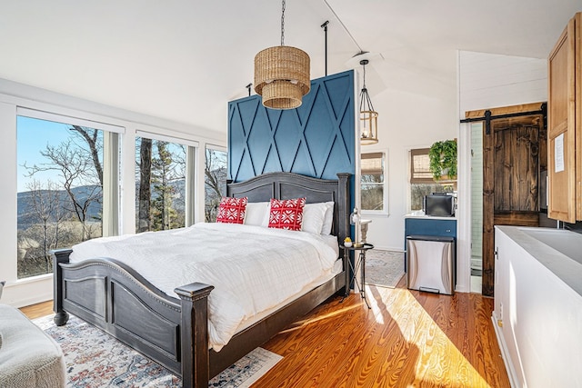 bedroom with multiple windows, wood-type flooring, a barn door, and lofted ceiling