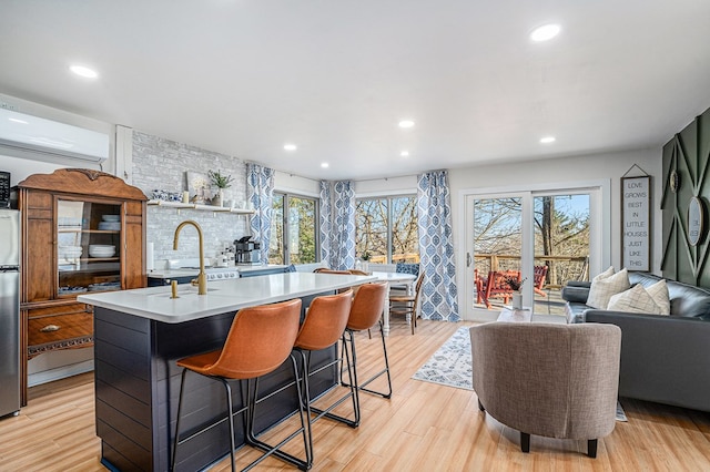 kitchen featuring a breakfast bar, sink, a center island with sink, a wall unit AC, and light hardwood / wood-style flooring