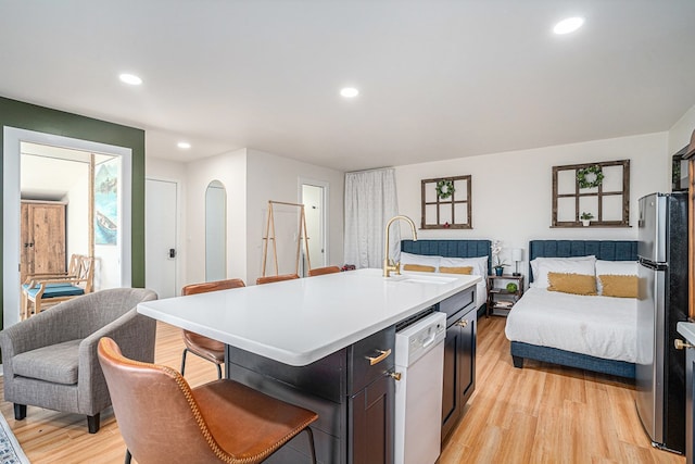 kitchen featuring sink, stainless steel fridge, white dishwasher, an island with sink, and light hardwood / wood-style floors