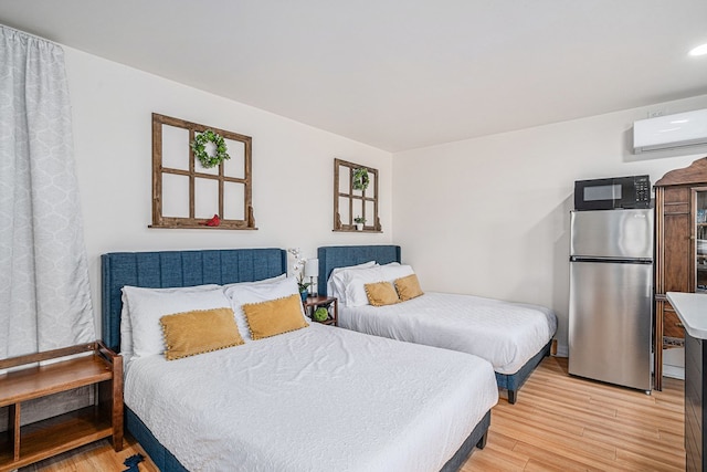 bedroom with an AC wall unit, stainless steel fridge, and light hardwood / wood-style floors