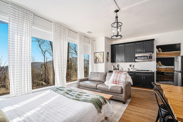 bedroom featuring a notable chandelier, stainless steel refrigerator, and light wood-type flooring