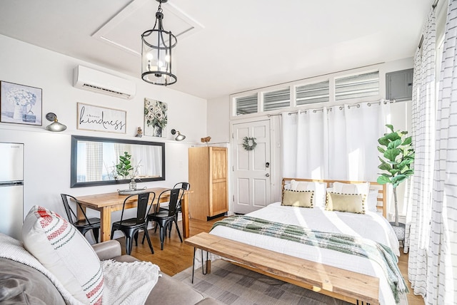 bedroom with an inviting chandelier, hardwood / wood-style floors, stainless steel fridge, and a wall unit AC