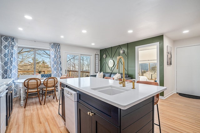 kitchen featuring sink, a breakfast bar, dishwasher, an island with sink, and light wood-type flooring