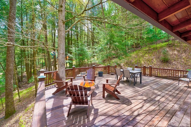 wooden deck featuring outdoor dining space, a forest view, and an outdoor fire pit